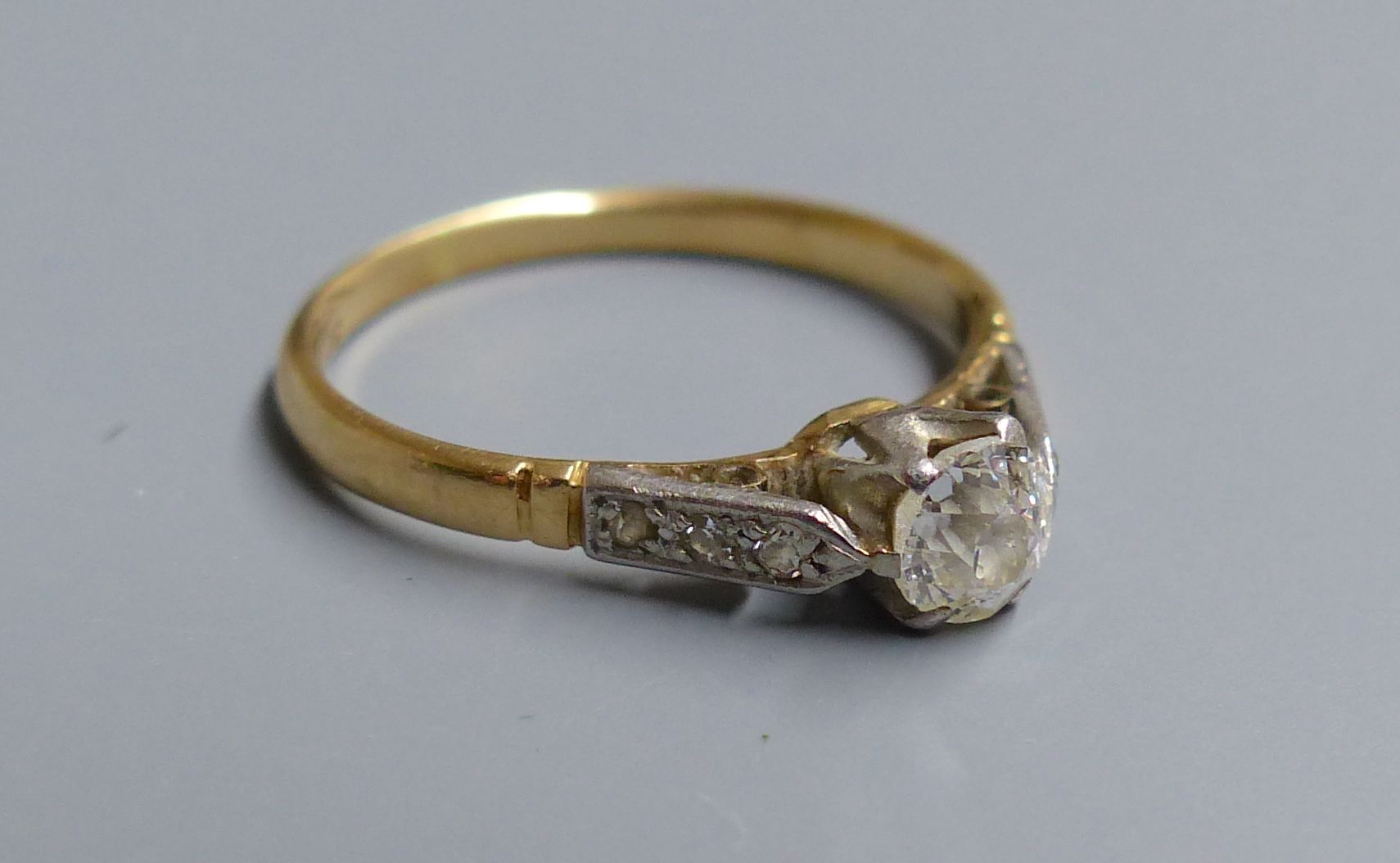 An 18ct and plat. single stone diamond ring, with diamond set shoulders, size I, gross 1.6 grams.